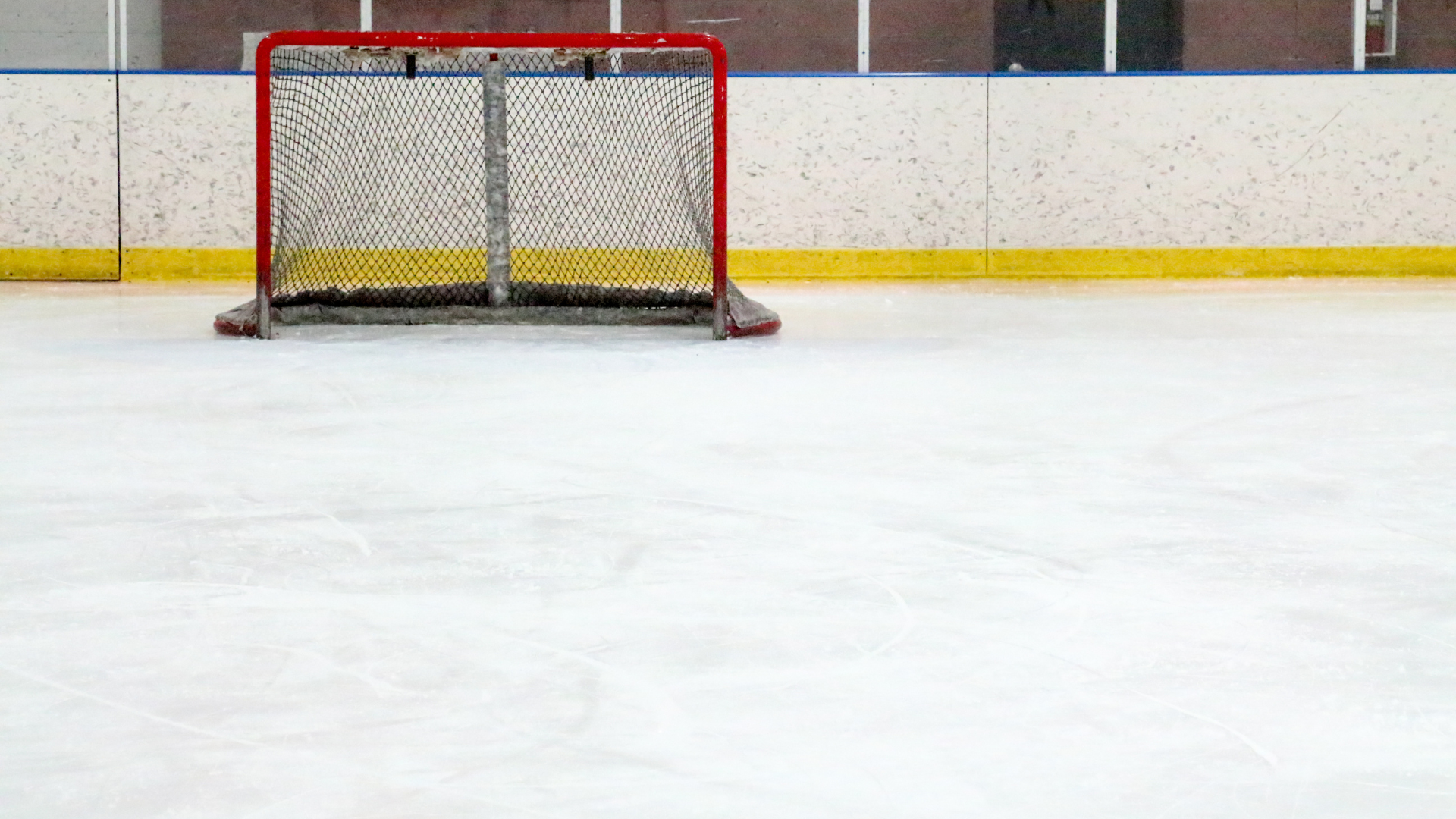 An empty hockey rink interior, the away bench visible across the ice